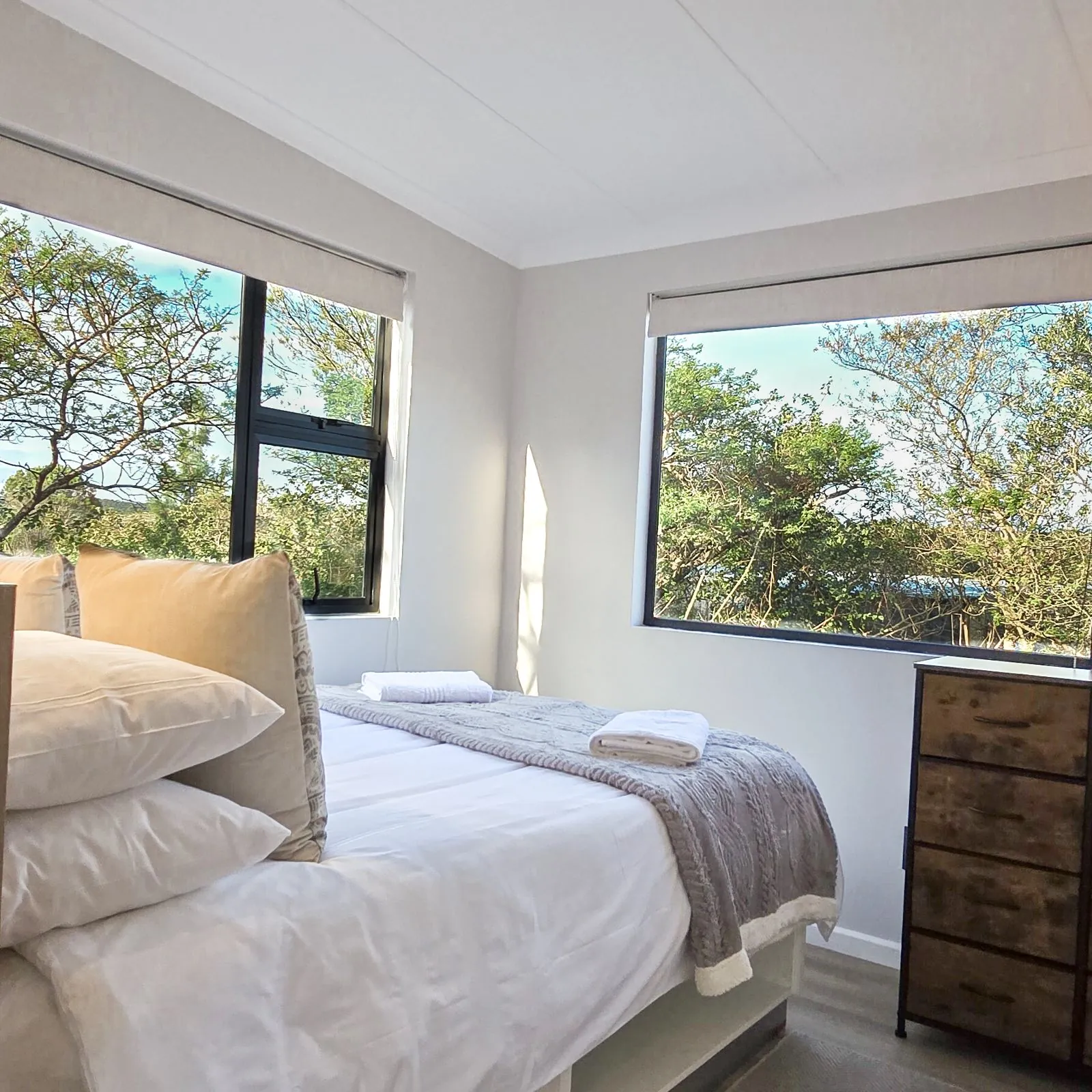 A bedroom with windows on two sides looking into the trees
